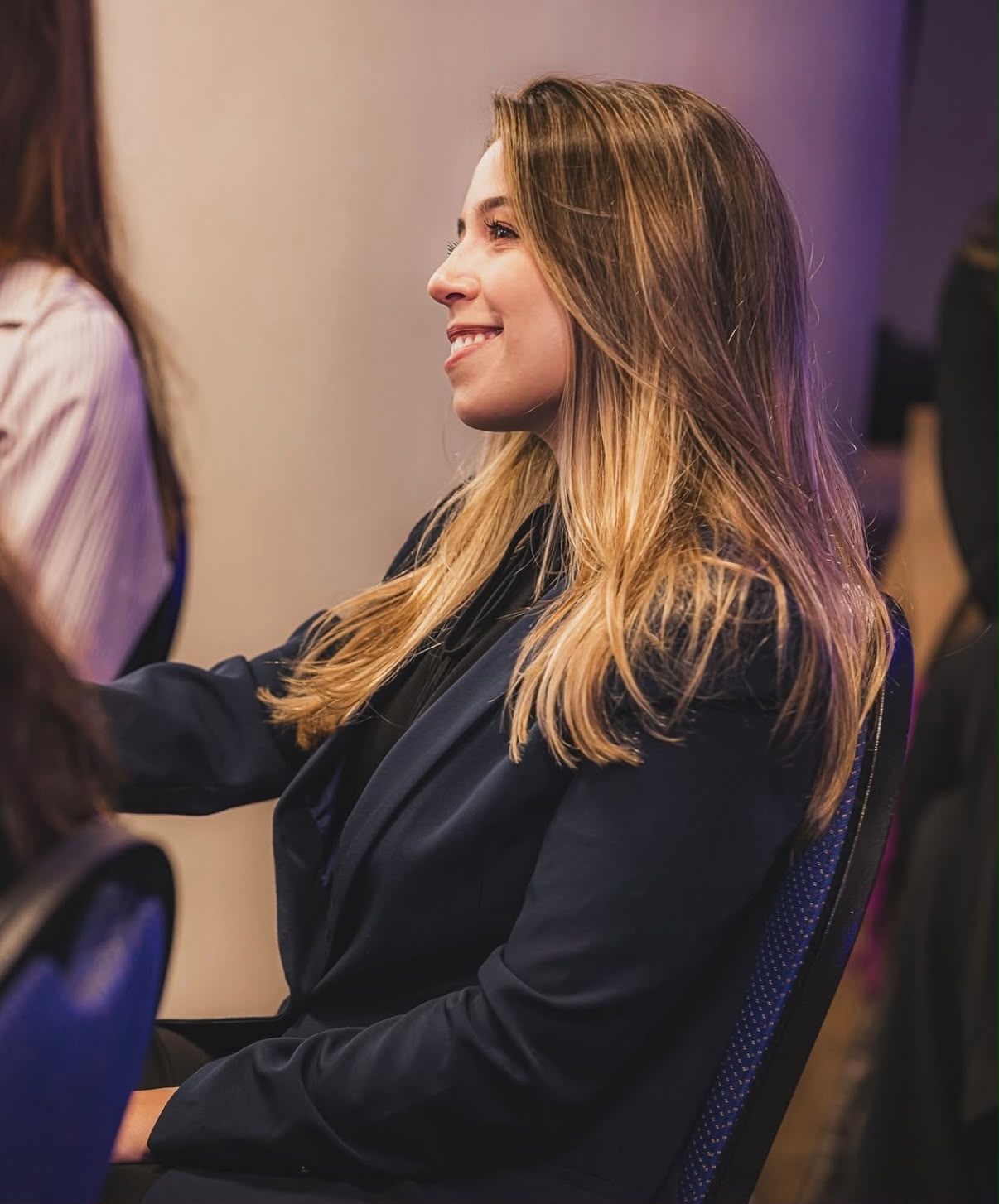Vitória Ourique de perfil, sorrindo, durante evento profissional.