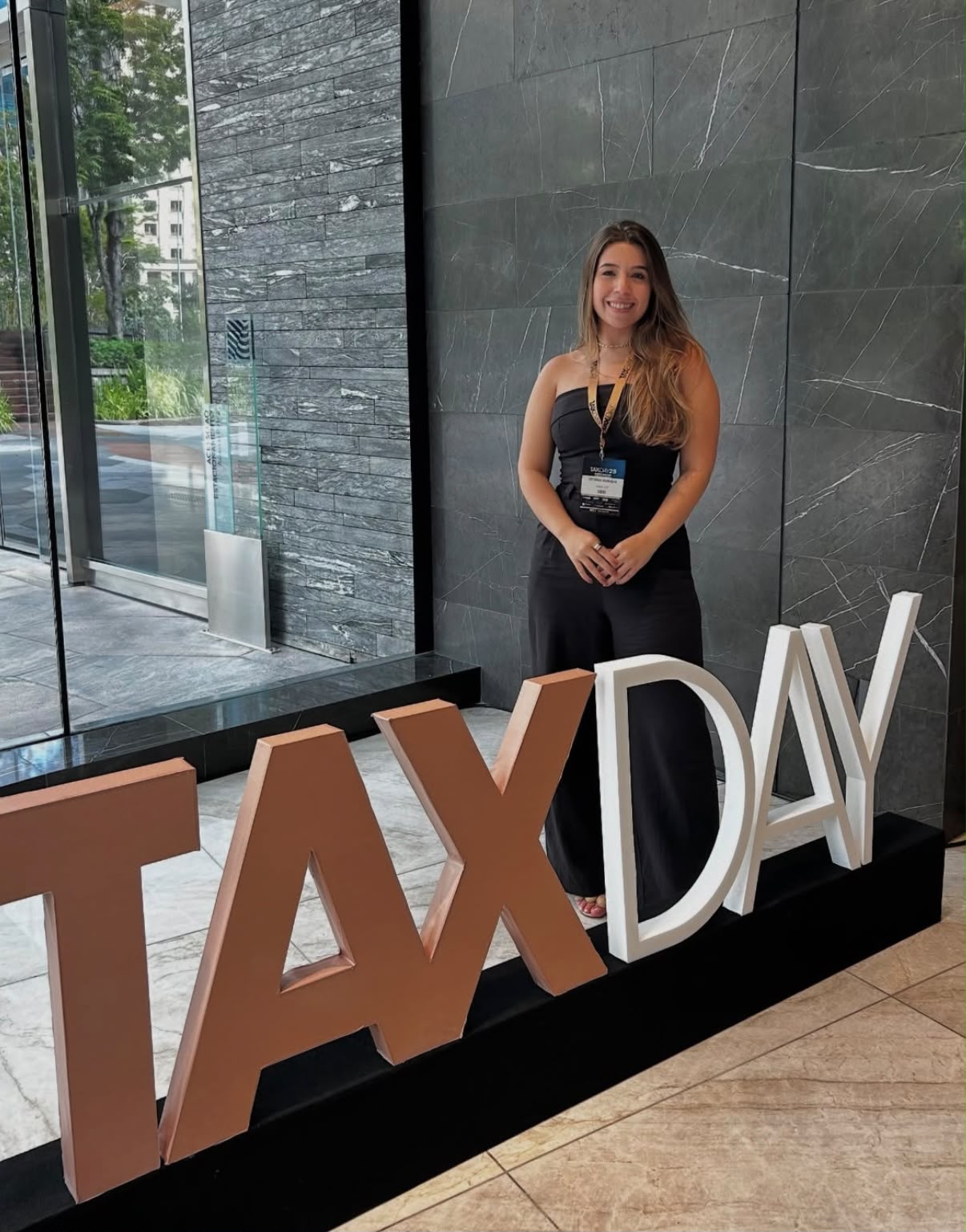 Vitória Ourique ao lado do painel do evento Tax Day 2025.